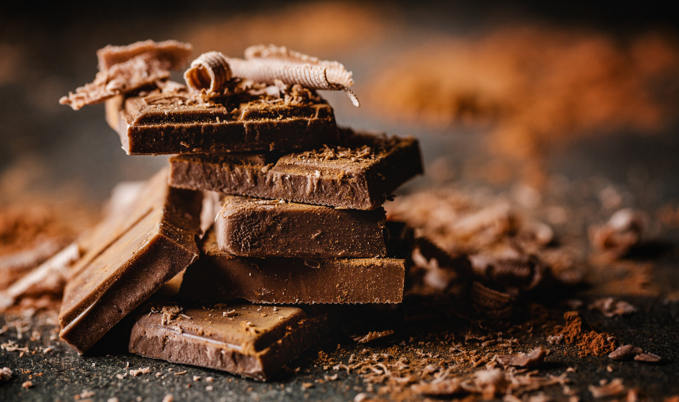 closeup shot of many squares of chocolate stacked one atop the other, with cocoa and chocolate shavings around them.