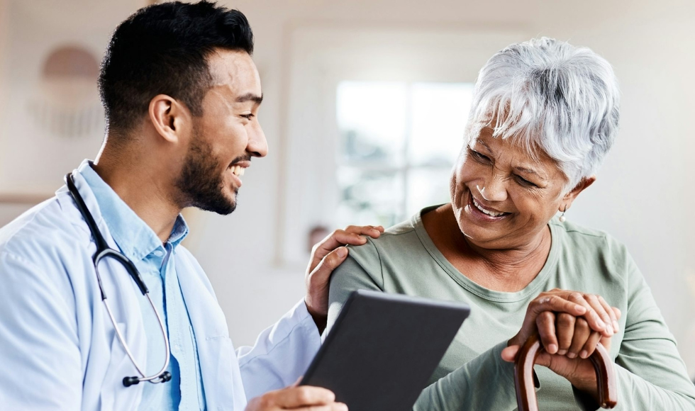 A smiling doctor puts his hand on a smiling patient's shoulder as they look at a report in his hand.