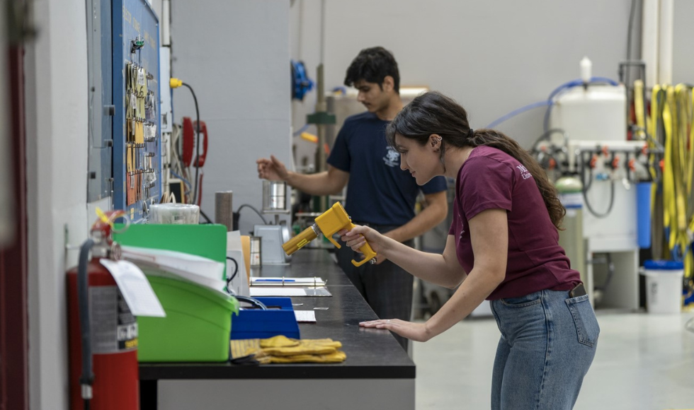 Two people working inside a nuclear reactor. One is pointing a device at an object that is set on a table.