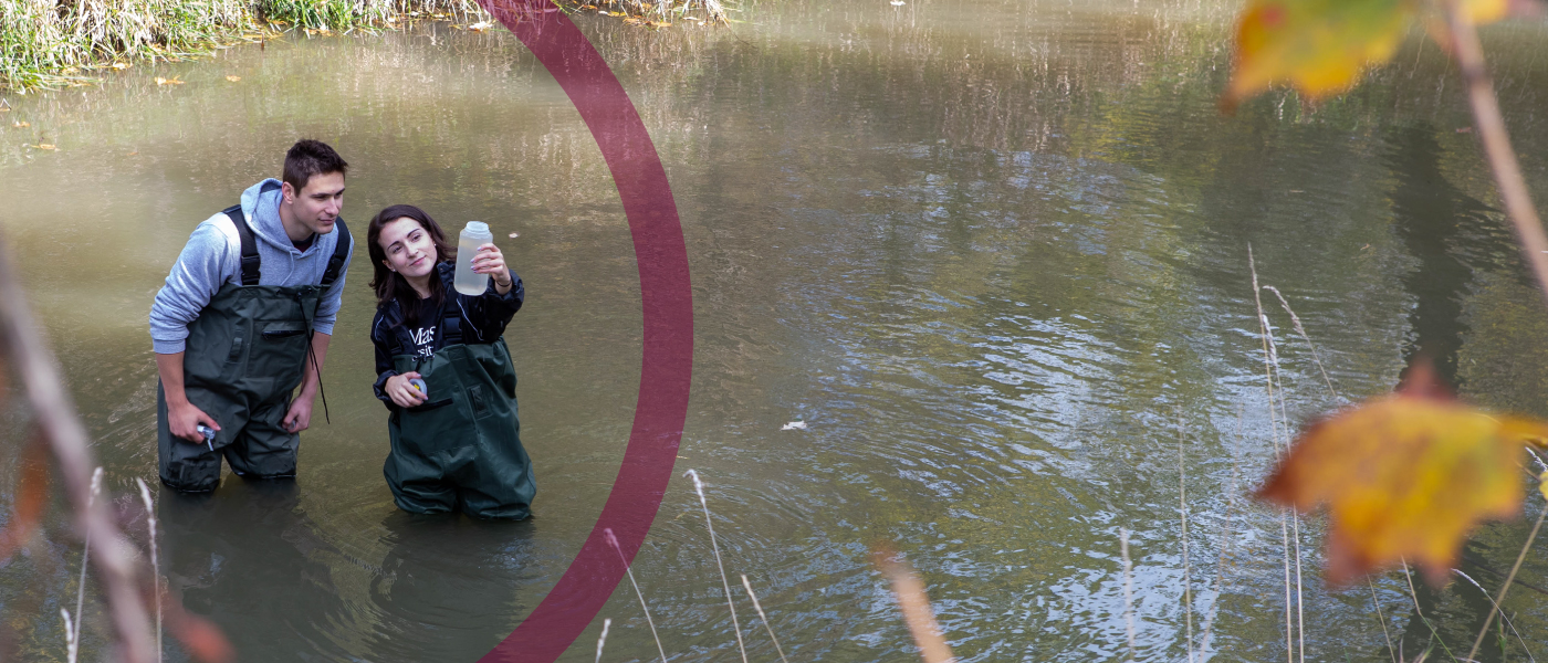 Two students stand in a lake, looking at a sample of the water.