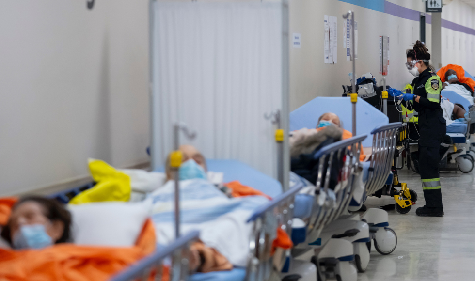 A first responder stands at the side of a patient on a hospital gurney, in a line of such patients on gurneys.