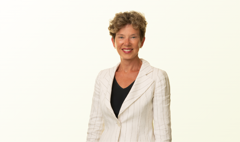 Head and shoulders of smiling Deborah Cook against a light backdrop, wearing a light-coloured blazer over a dark v-neck top.