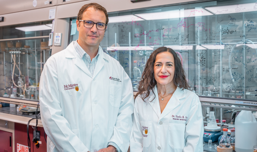 Two people in white lab coats standing side-by-side looking directly at the camera.