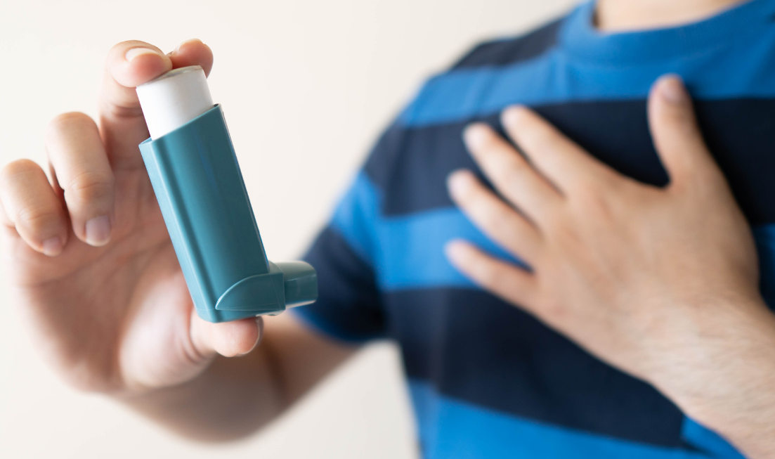 A closeup of an asthma inhaler or puffer, held in one hand while the person's other hand is on their chest.