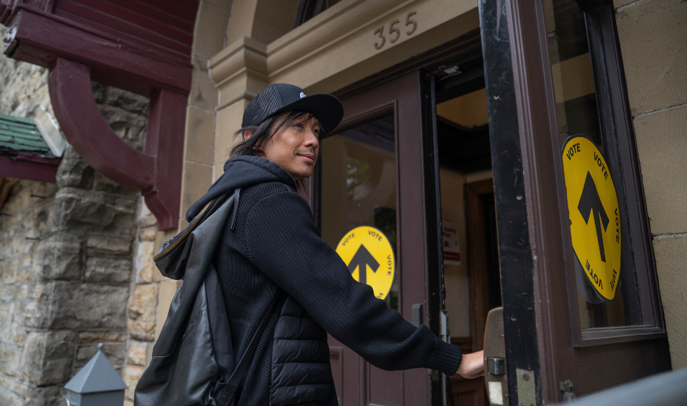 A person has their hand on the open door, about to enter a building marked as a polling location.