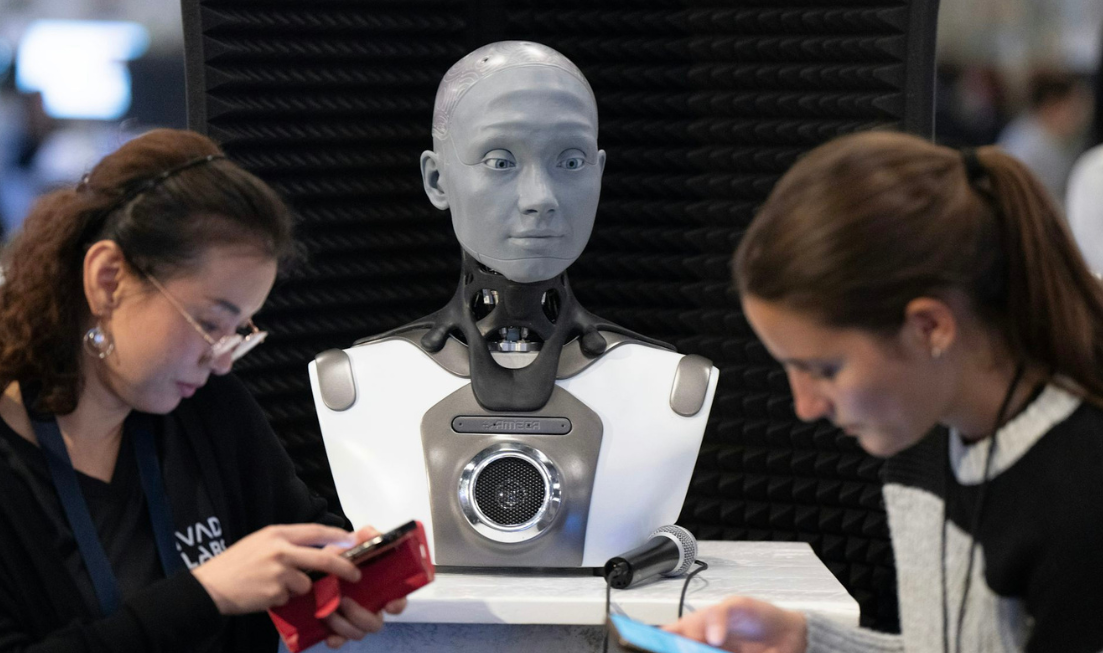 Two people look down at their smartphones standing in front of a grey human-like robot.