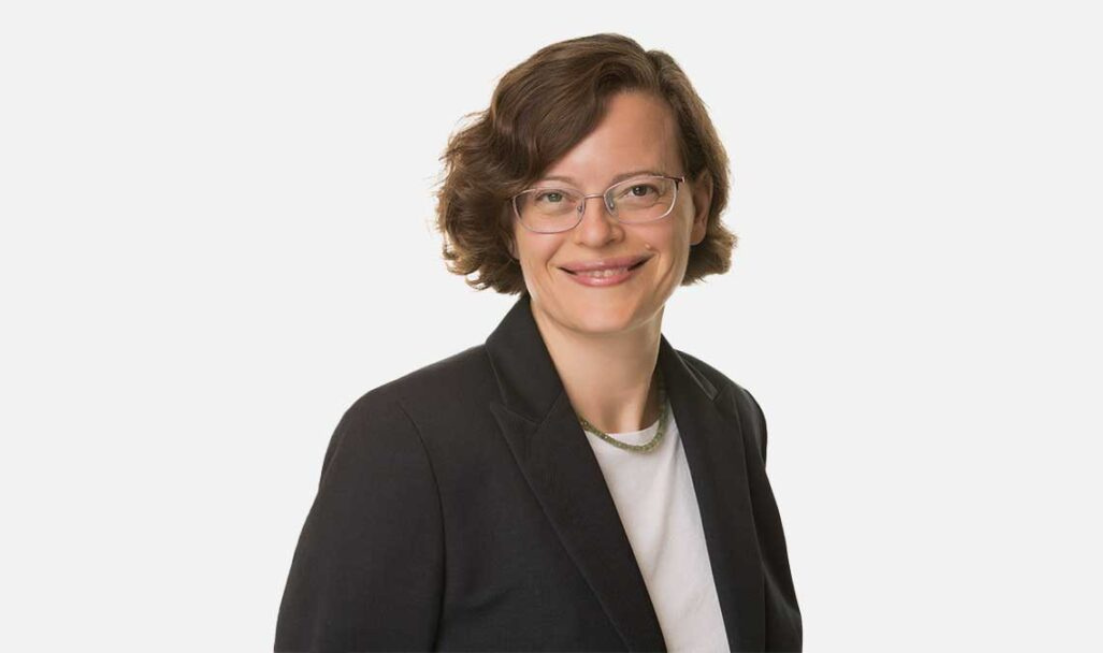 Head and shoulders of Katherine Zukotynski wearing a white top, necklace, black blazer and glasses, smiling at the camera.