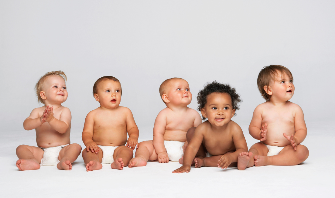 Five babies in white diapers, sitting in a row against a light backdrop.